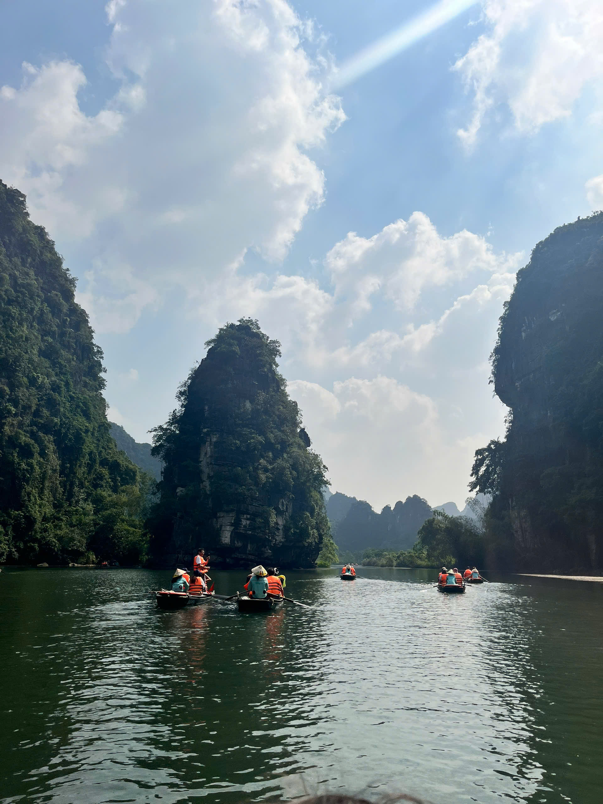 Thuyền rẽ sóng giữa thung lũng núi đá, trời trong mây nhẹ
